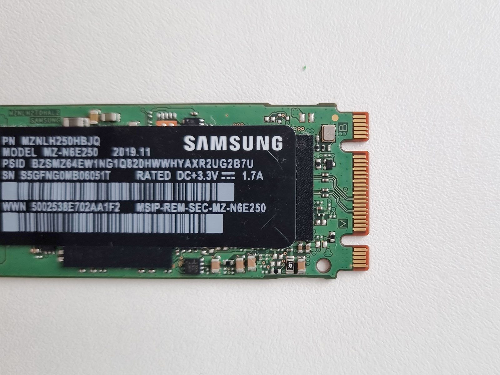 Back of an M.2 SSD circuit board, showing the controller chip, flash memory package, and gold connector edge.